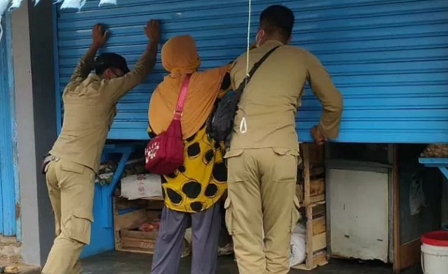 Seorang pedagang di Pasar Kliwon Temanggung menutup kios lebih awal dibantu petugas Satpol PP pada pelaksanaan PPKM darurat hari pertama,